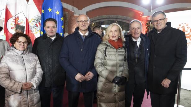 Sechs Menschen tragen Jacken und stehen vor beleuchtetem Gebäude