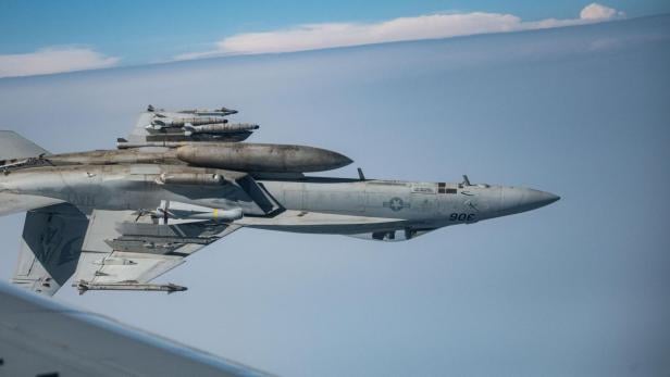 Kampfjet F/A-18 fliegt mit Bewaffnung und Zusatztanks am Himmel.