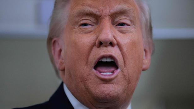 Donald Trump spricht mit geöffnetem Mund und trägt einen dunklen Anzug mit Krawatte.