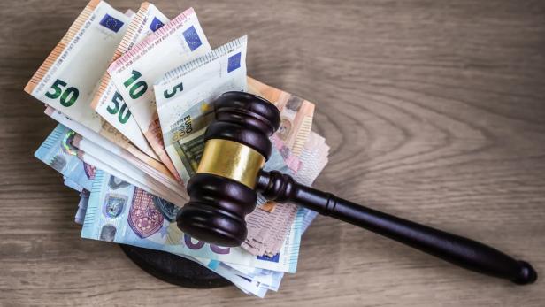 Ein Richterhammer liegt auf einem Stapel verschiedener Euro-Geldscheine auf einer Holzoberfläche.