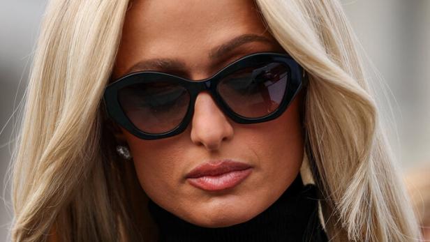 Paris Hilton mit Sonnenbrille und schwarzem Rollkragenpullover blickt in die Kamera.