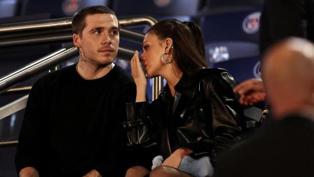 Brooklyn Beckham und Nicola Peltz sitzen nebeneinander. Sie flüstert ihm etwas ins Ohr, während er aufmerksam zuhört.