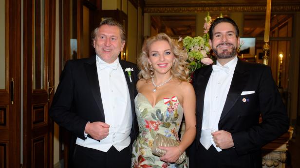 Drei elegant gekleidete Personen posieren lächelnd nebeneinander, zwei Männer im Frack und eine Frau im floralen Abendkleid.