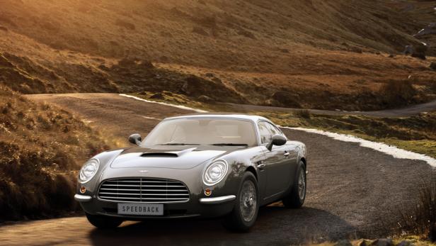 Ein grauer David Brown Speedback GT auf einer Landstraße vor einer hügeligen Landschaft.