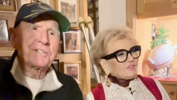 Prinz Frédéric von Anhalt sitzt mit Rosi Schipflinger auf einer Bank, im Hintergrund sind Krücken zu sehen.