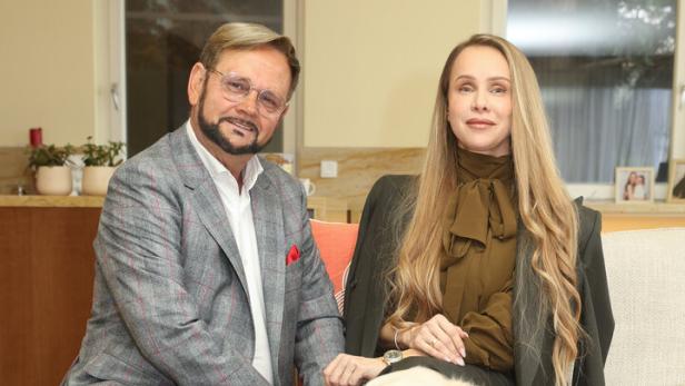 Ein Mann und eine Frau sitzen auf einem Sofa, vor ihnen ein großer, heller Hund und ein Blumenstrauß auf dem Tisch.