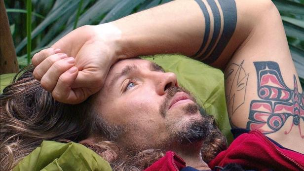 Gil Ofarim liegt auf dem Rücken und legt sich den linken Handrücken auf die Stirn