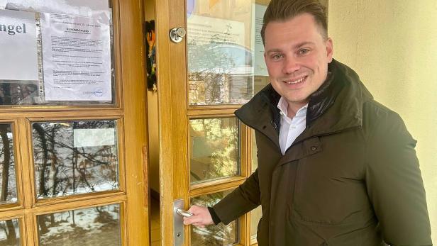 Ein Mann in Jacke öffnet die Tür zu einem Wahllokal, an der Aushänge befestigt sind.