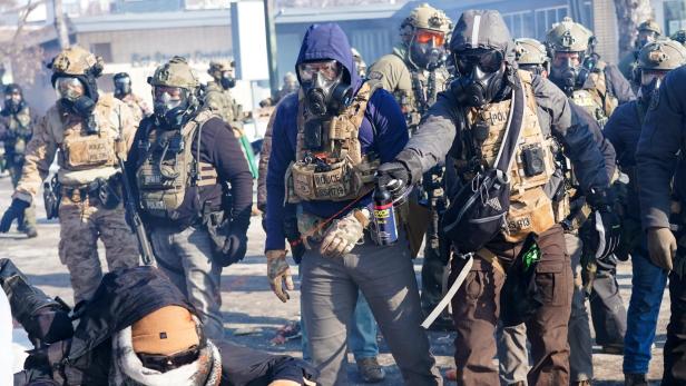 Eine Gruppe von Polizisten in Schutzausrüstung steht auf einer Straße, während eine Person am Boden kauert.