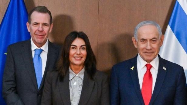 Drei Personen posieren vor Flaggen und dem Staatswappen Israels, darunter Benjamin Netanjahu mit roter Krawatte.