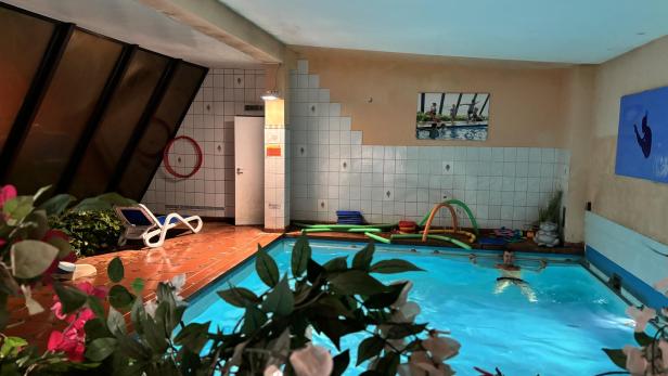 Ein Mann schwimmt in einem hell erleuchteten Innenpool mit Schwimmhilfen am Beckenrand.