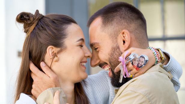 Ein Paar lächelt sich an, sie hält einen herzförmigen Schlüsselanhänger mit Foto.