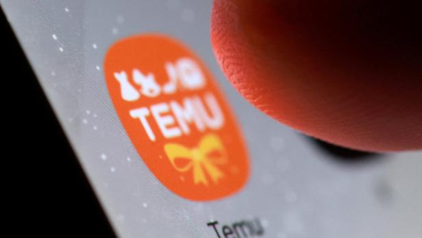 Ein Finger berührt das orangefarbene Temu-App-Symbol mit weißer Schrift und einer gelben Schleife auf einem Smartphone-Bildschirm.
