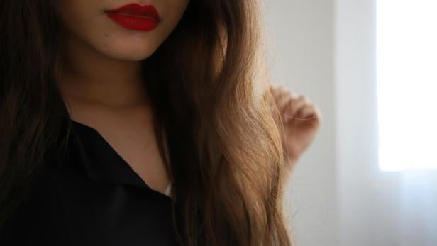 Frau mit langen, gepflegten Haaren und rotem Lippenstift vor hellem Hintergrund.