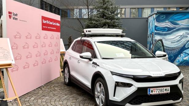 Ein weißes Auto mit Scan-Technik auf dem Dach steht vor einer pinken Wand mit Stadt Wien Logo und Illustrationen.