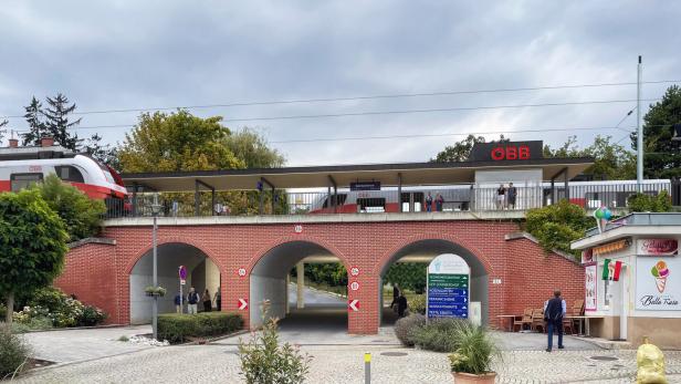 Ein ÖBB-Zug fährt über eine rote Backsteinbrücke mit Durchgängen, neben einem Platz mit einem Eisstand namens "Bella Rosa".