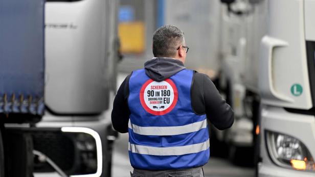 Ein Mann mit Warnweste und Aufdruck zwischen zwei Lastwagen auf einer Straße.