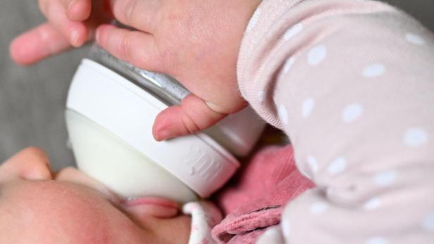 Ein Baby trinkt Milch aus einer Babyflasche und hält sie mit seinen Händen fest.