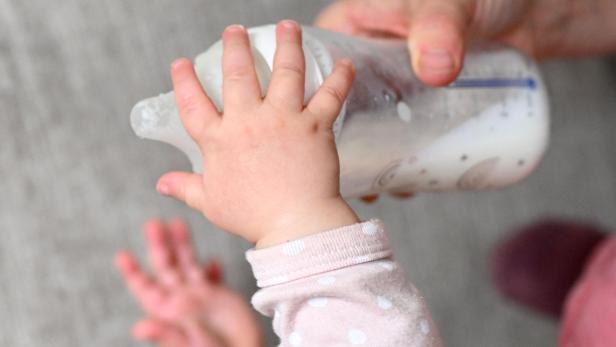 Ein Baby greift nach einer mit Milch gefüllten Flasche, die von einer erwachsenen Hand gehalten wird.
