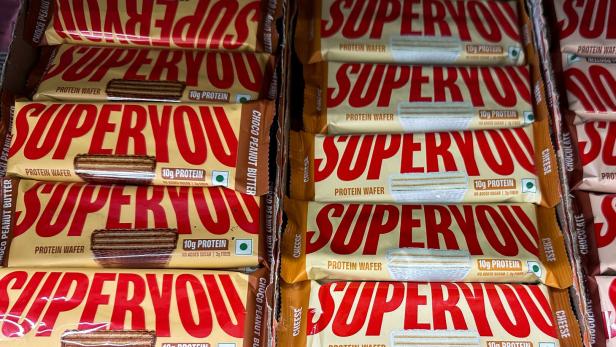 Mehrere Proteinwaffeln mit der Aufschrift „SUPERYOU“ in zwei Geschmacksrichtungen, ordentlich in Kartons gestapelt.