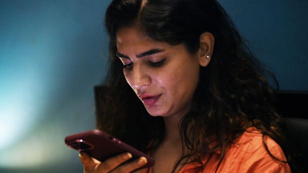 Eine Frau mit langen dunklen Haaren hält ein Smartphone und spricht konzentriert hinein.