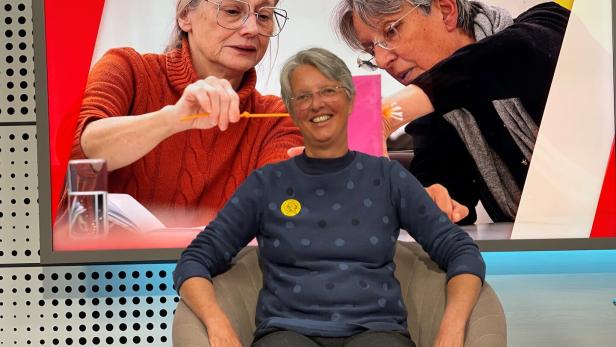 Sabine Martin-Jell sitzt im KURIER-TV-Studio vor einem Foto von Science Omas.