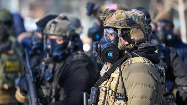 Mehrere Polizisten mit Gasmasken und taktischer Ausrüstung stehen im Freien.