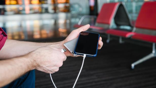 Eine Person hält ein Smartphone und eine Powerbank in der Hand und verbindet sie mit einem Ladekabel.