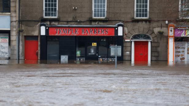 Eine Straße mit starkem Hochwasser, das bis zu den Türen eines Friseursalons und angrenzender Gebäude reicht.
