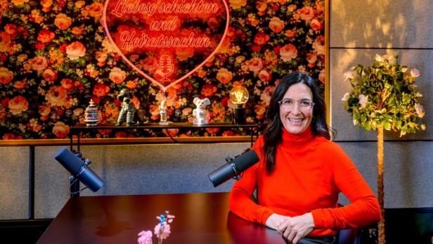 Liebesg'schichten und Heiratssachen - Der Podcast: Nina Horowitz sitz an einem Tisch hinter einem Podcastmikro.