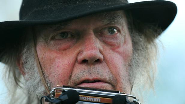 Neil Young mit schwarzem Hut spielt eine Mundharmonika.