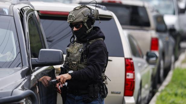 Ein Polizist in taktischer Ausrüstung öffnet die Tür eines dunklen SUVs.