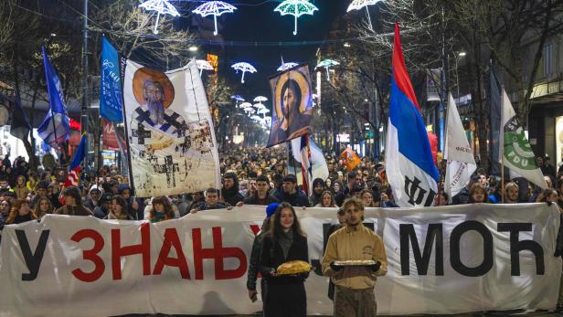 Viele Menschen marschieren nachts mit Fahnen, religiösen Ikonen und einem großen Banner durch eine beleuchtete Straße.