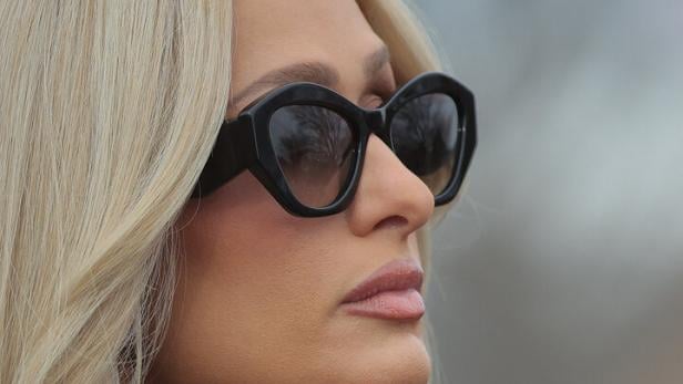 Paris Hilton mit Sonnenbrille und schwarzem Rollkragenpullover blickt zur Seite.