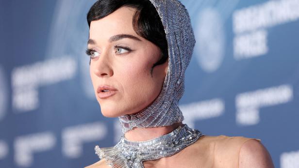 Katy Perry mit silbernem, glitzerndem Kopfschmuck und passendem Halsband vor blauem Hintergrund.