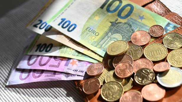 Mehrere Euro-Geldscheine und Münzen liegen auf einer braunen Geldbörse.