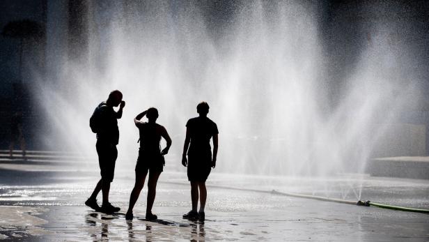 Drei Personen stehen vor einem großen Wasserstrahl, der aus mehreren Düsen aufsteigt.