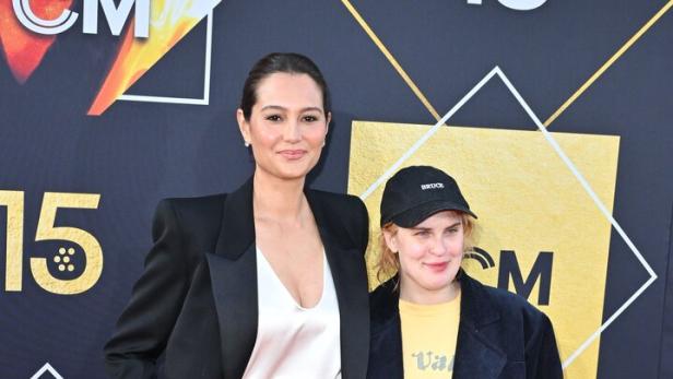 Emma Heming Willis und Tallulah Willis stehen nebeneinander auf einem roten Teppich, Emma elegant im Anzug, Tallulah leger mit Basecap und zerrissener Hose.