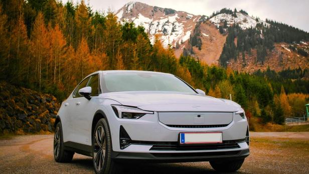 Ein weißes E-Auto steht auf einer Straße, dahinter ist herbstliche Landschaft zu sehen