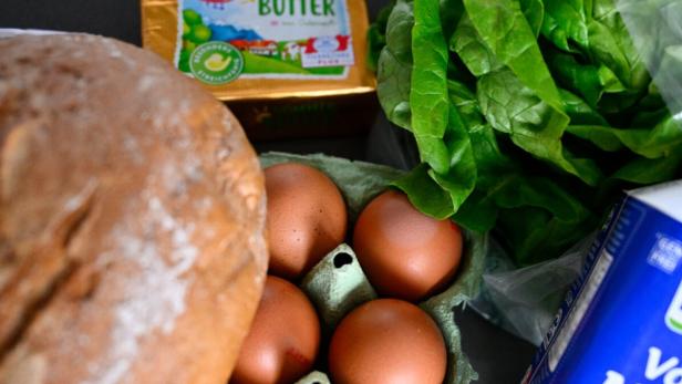 Ein Laib Brot, braune Eier, ein Salatkopf, Butter und eine Packung Milch liegen nebeneinander.