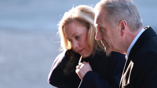 Bettina Wulff mit ernstem Gesichtsausdruck steht im Freien bei kühlem Wetter.