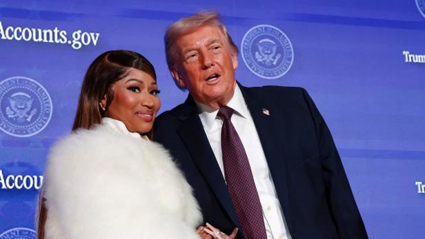 Donald Trump posiert mit Nicki Minaj, die eine weiße Pelzjacke trägt, vor einem blauen Hintergrund. Sie stehen Hand in Hand.