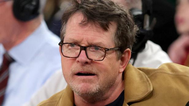 Michael J. Fox sitzt mit Brille und brauner Jacke im Publikum.