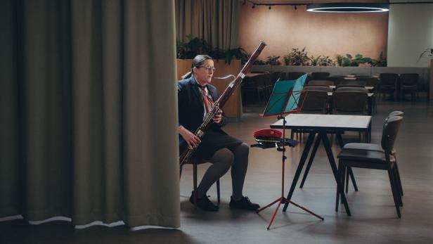 Eine Frau sitzt in einem großen Raum auf einem Stuhl und spielt mit ihrem Instrument.