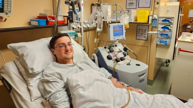 Ein junger Mann liegt im Krankenhausbett und ist an medizinische Geräte zur Blutbehandlung angeschlossen.