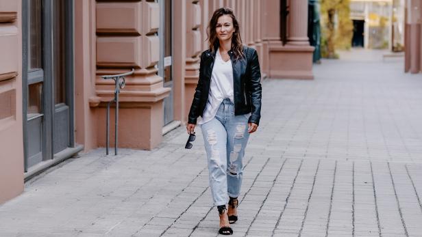 Eine Frau in Jeans und Lederjacke läuft eine Straße lang 