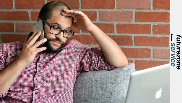 Ein Mann sitzt vor einem Laptop und telefoniert