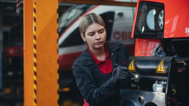 Eine Frau in einer Werkstatt schraubt an einer Zuggarnitur.