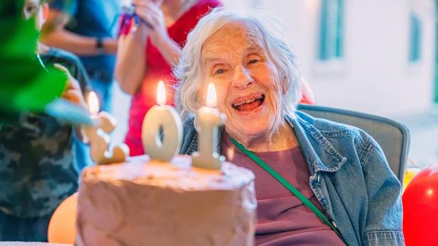 Smiling, Excited Elderly Woman Looks to the "103" Birthday Candles on a Cake