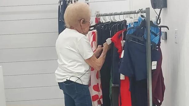 92-jährige Frau mit weißem T-Shirt steht vor einer Kleiderstange mit Kleidung